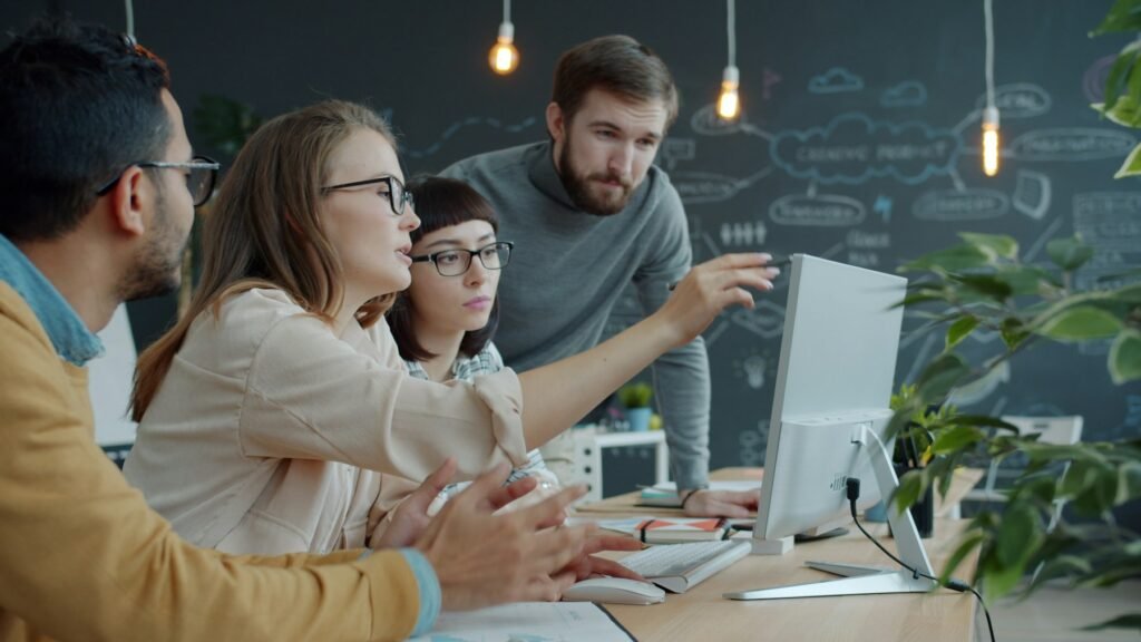 Colleagues working together around a laptop in an open plan office